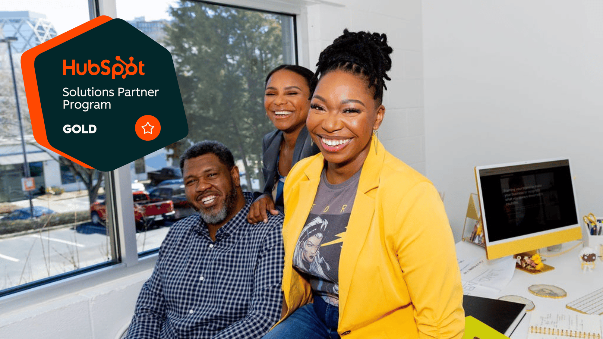 Photo of Framework Marketing Consulting Team (1 man, 2 women) sitting on desk in front of a window overlooking The Lola Co-working Space parking lot